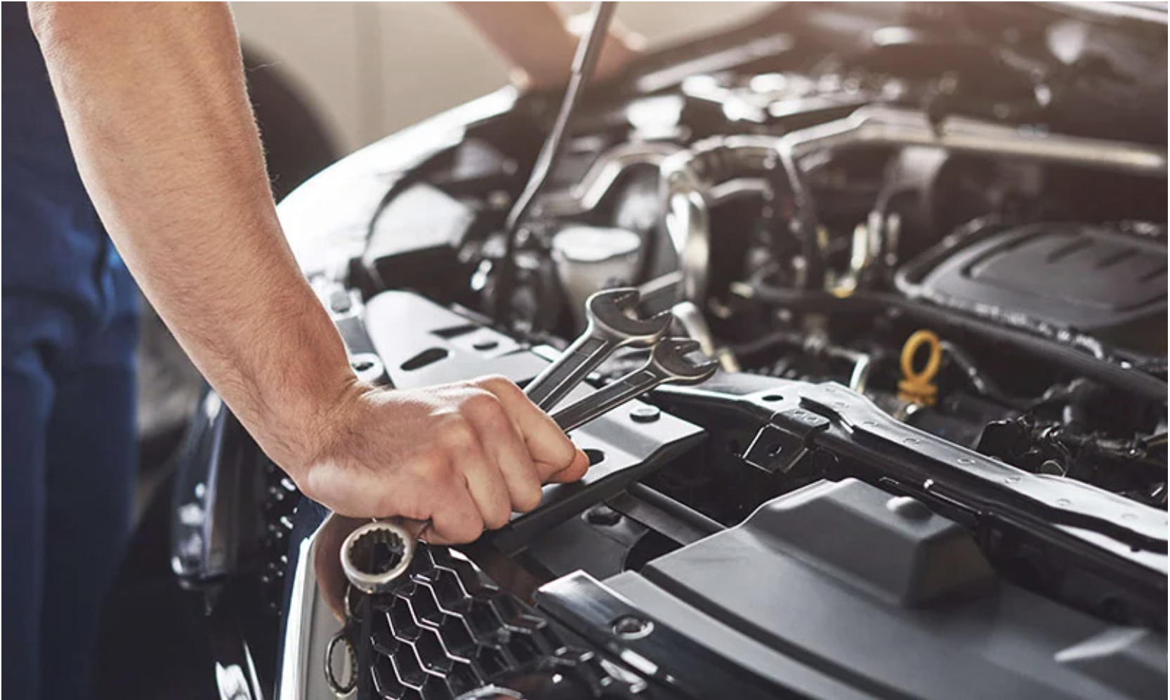 Automotive maintenance close-up with a hand tool over an engine bay.